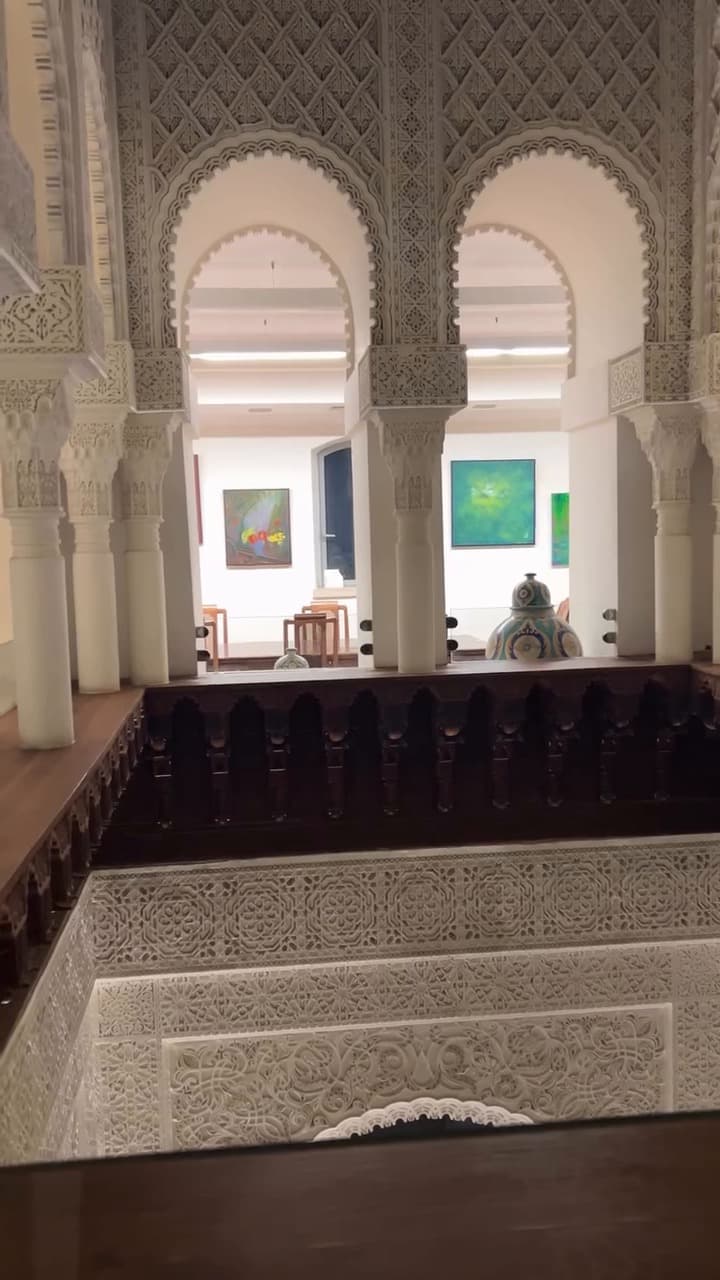 Paintings on white walls seen through carved Moroccan-style arches at the Échappées belles exhibition