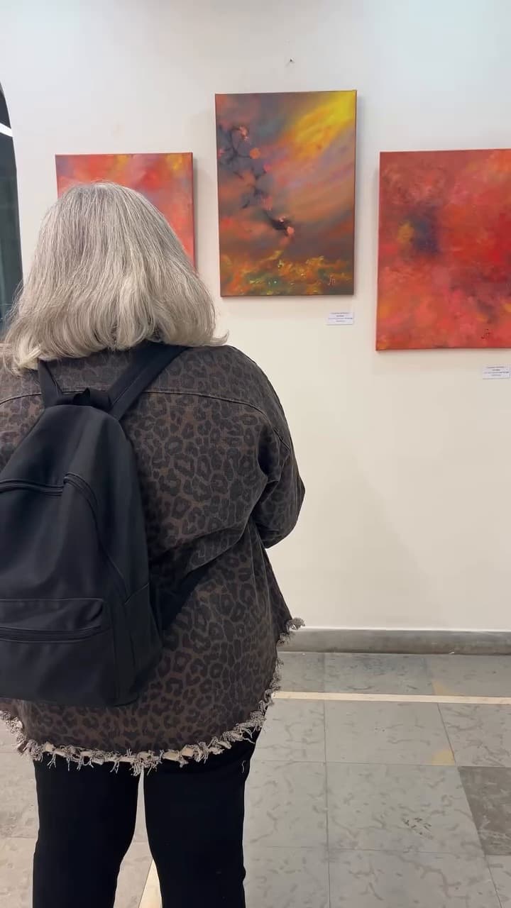 Visitor seen from behind looking at three red and orange paintings at the Échappées belles exhibition