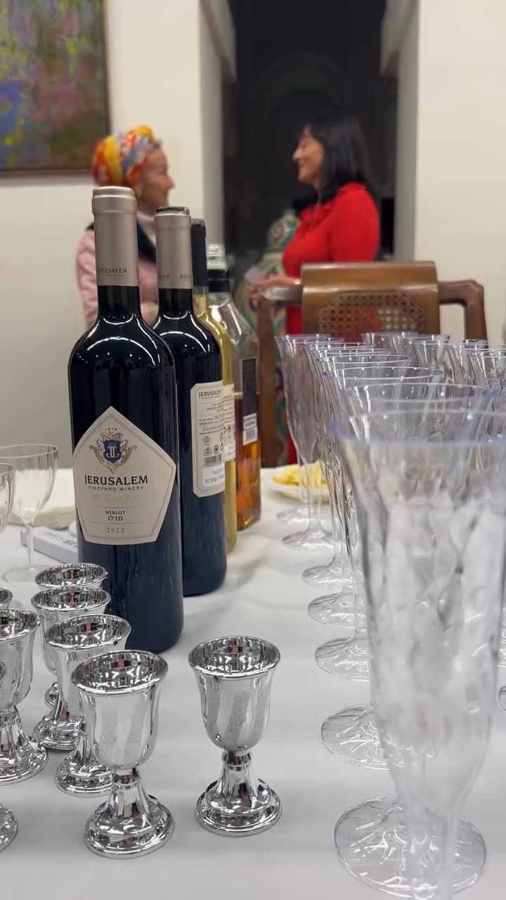 Reception table with red wine bottles, silver kiddush cups and glasses, guests in the background